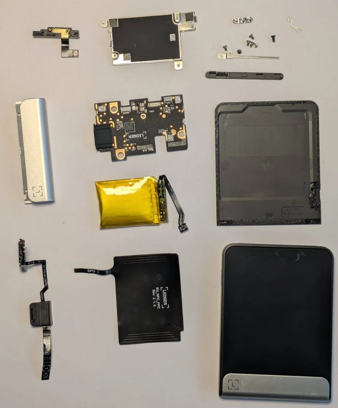 Ledger Flex desmontada com os componentes internos oficiais: bateria, antena NFC, placa de circuito e tela